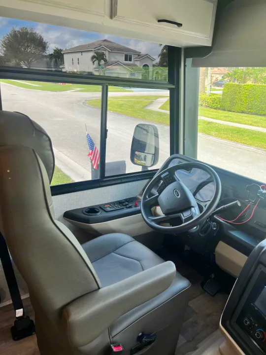 Inside a spacious RV rental: driver's seat, Ford steering wheel, and a clear view of a suburban street.. Entegra Vision 2023