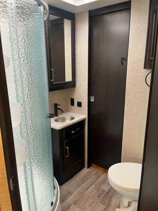 Compact RV rental bathroom featuring a shower, vanity with sink, medicine cabinet, and toilet. Perfect for travel.. Entegra Vision 2023
