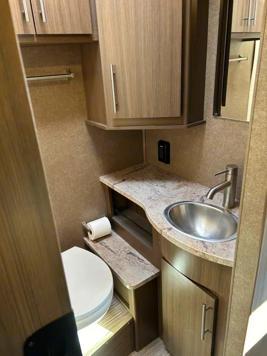 Experience comfort in your RV rental with this compact bathroom featuring a toilet, sink, mirror, and wood cabinets.. Thor Motor Coach Vegas 2018