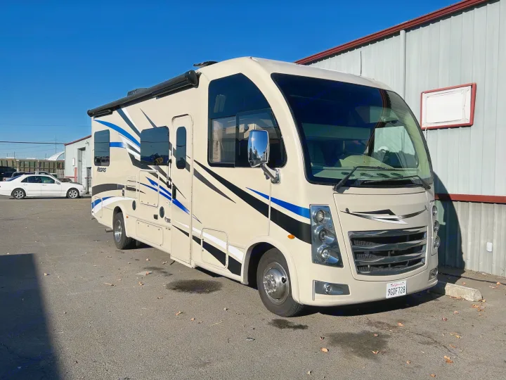 A cream Thor Vegas Class A motorhome, featuring blue and black stripes, stands ready for rv rental, parked on asphalt beside a building.. Thor Motor Coach Vegas 2018