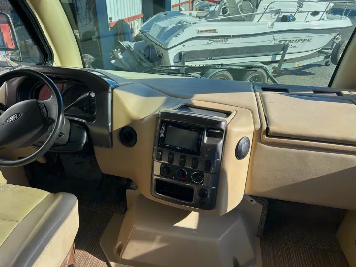 Inside an RV rental: driver's area with tan dashboard, steering wheel. A boat on a trailer is seen through windshield.. Thor Motor Coach Vegas 2018
