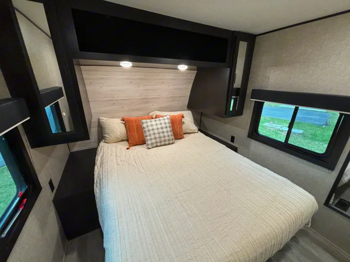 Cozy RV rental bedroom features a comfortable bed with throw pillows, overhead storage, and dual windows. Ideal for travel.. Jayco Jay Flight 2023