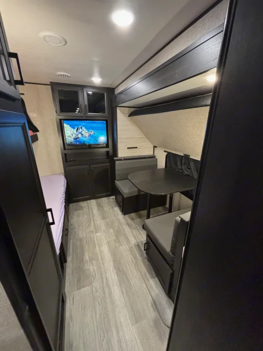 View of a cozy RV rental interior, showcasing a dinette, TV, bunk beds, and light wood-look flooring.. Jayco Jay Flight 2023