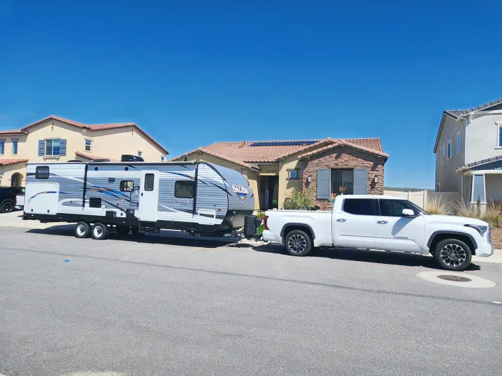 White pickup truck towing an RV rental (travel trailer) on a sunny residential street. Ideal for camping & travel.. Forest River Salem 2019