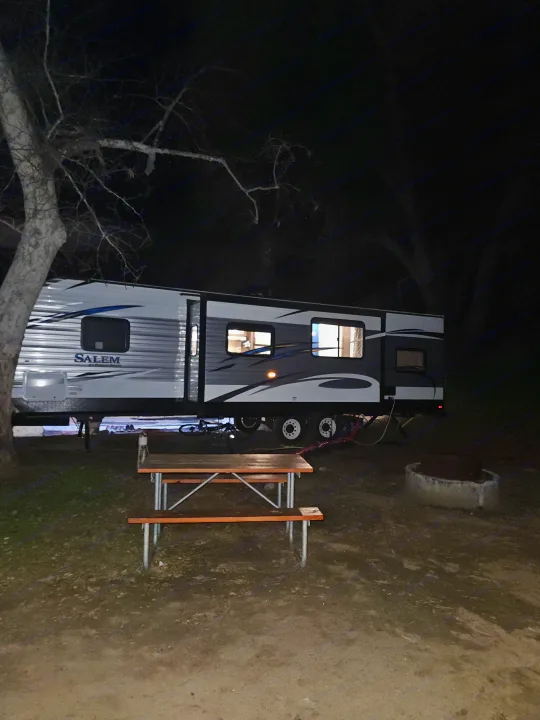 Nighttime rv rental setup at a peaceful campsite with a picnic table and fire pit under dark trees.. Forest River Salem 2019