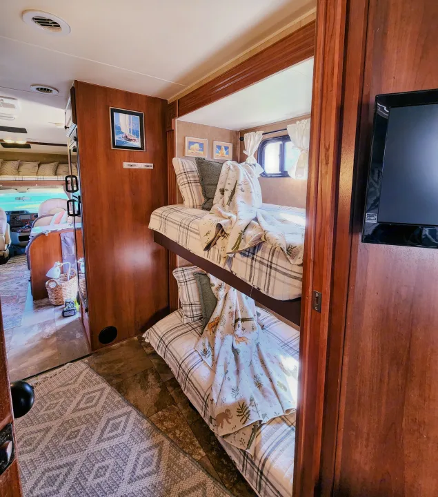 Explore a comfortable RV rental interior with cozy bunk beds, a plaid theme, and a TV, great for family adventures.. Coachmen Leprechaun 320BH 2014
