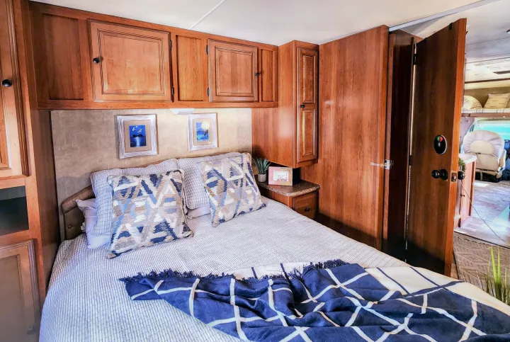 Cozy RV rental bedroom featuring wood cabinets, comfy bed, decor, and door to living space. Ideal for travel.. Coachmen Leprechaun 320BH 2014