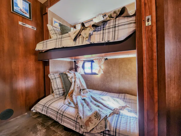 RV rental interior: cozy bunk beds with plaid bedding & a nature-themed blanket, ideal for family travel.. Coachmen Leprechaun 320BH 2014