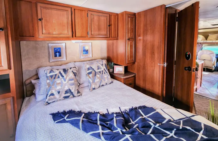 RV rental interior: A cozy bedroom with overhead wooden cabinets, a striped bed, and decorative pillows.. Coachmen Leprechaun 320BH 2014