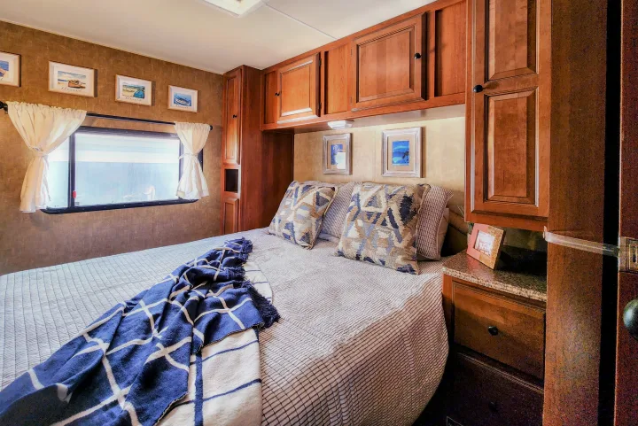 This cozy RV rental bedroom features a comfortable bed with striped comforter, ample wood cabinets, and coastal-themed wall art.. Coachmen Leprechaun 320BH 2014