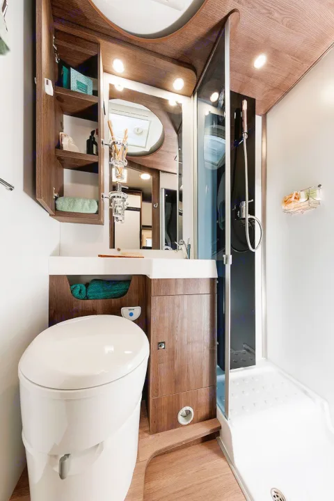 Compact RV rental bathroom with wood accents, including toilet, sink, mirror, and integrated shower. Modern and space-saving.. Benimar Sport 340 UP 2024