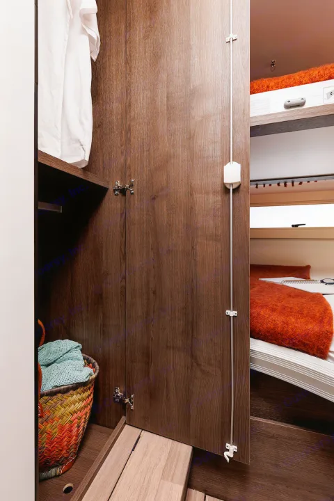 Cozy RV rental interior with an open wooden wardrobe showing clothes & basket, next to a bed with a bright orange blanket.. Benimar Sport 340 UP 2024
