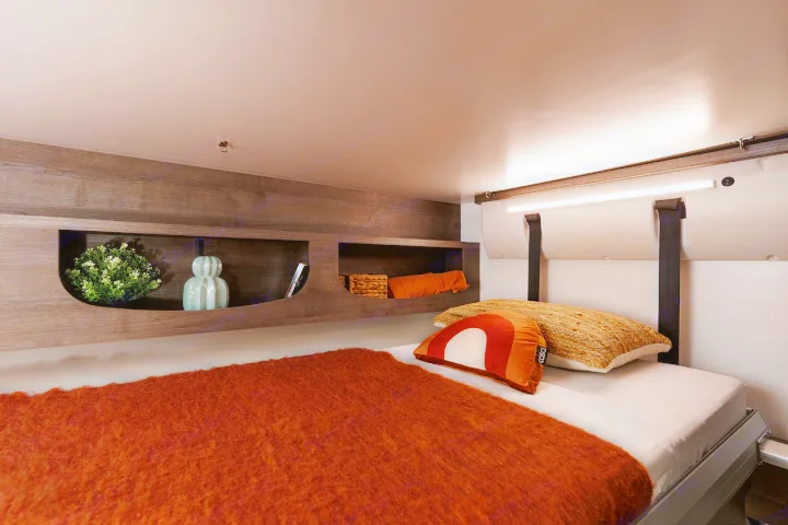 Cozy RV rental bedroom with warm orange bedding, integrated shelving, and LED lighting for comfortable travel.. Benimar Sport 340 UP 2024
