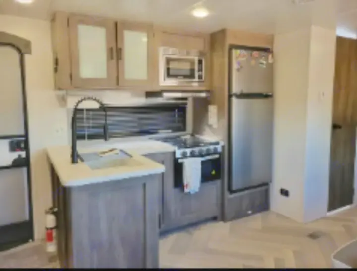 Modern RV rental kitchen with stainless steel fridge, range, microwave, and island sink. Ready for travel adventures.. Forest River Wildwood 2022