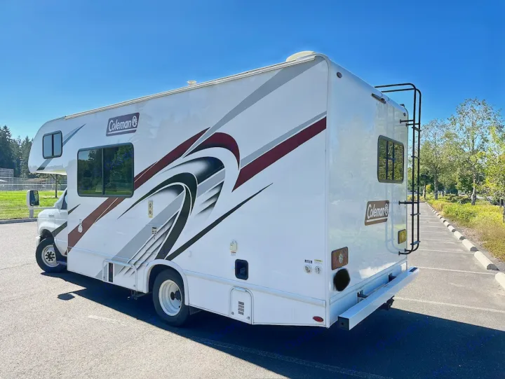 Explore the outdoors with this white Coleman RV rental. This motorhome features graphics and a rear ladder, parked on asphalt.. Coleman 22EQ 2022