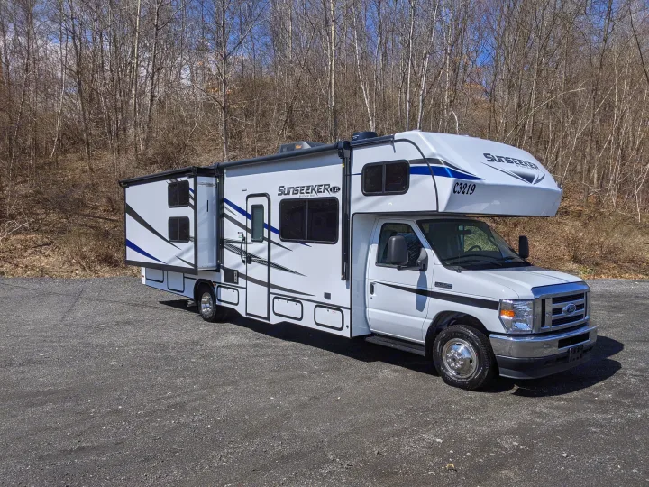 This white Class C Sunseeker motorhome, a perfect RV rental option, is shown parked on a gravel lot against bare trees.. Forest River Sunseeker 2025