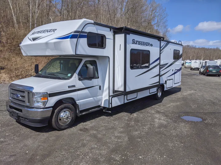 A white Sunseeker Class C motorhome, ideal for RV rental, parked on an asphalt lot with other RVs under a blue sky.. Forest River Sunseeker 2025
