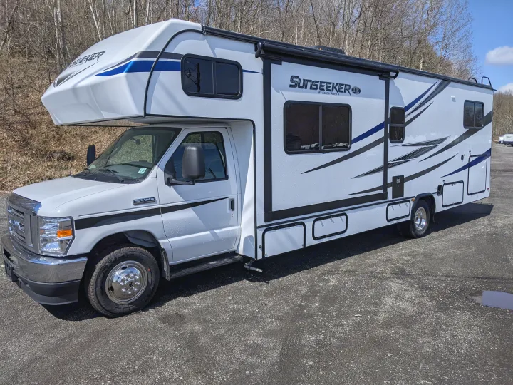 White Forest River Sunseeker E-450 RV rental, a Class C motorhome with blue & black accents, parked on asphalt.. Forest River Sunseeker 2025