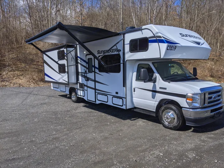 White Sunseeker RV rental with an extended slide-out and awning, parked on a gravel surface.. Forest River Sunseeker 2025