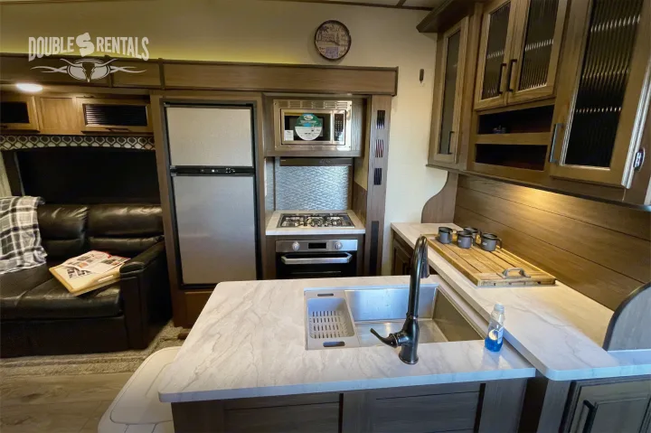 Modern rv rental interior: kitchen with fridge, stove, oven, microwave, sink, and a comfy sofa in the living area.. Prime Time Crusader Lite 2020