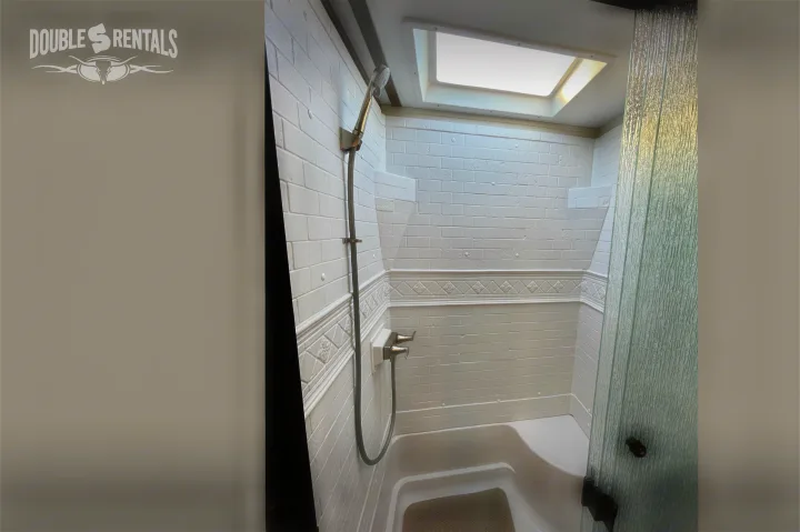 Inside a compact RV rental shower: white brick-patterned walls, a hand-held shower, skylight, and textured glass door.. Prime Time Crusader Lite 2020