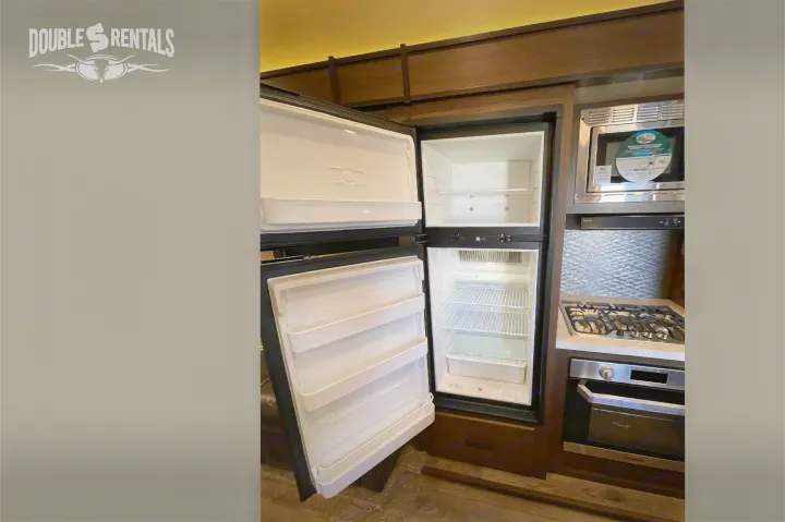 RV rental: Open, empty refrigerator, microwave, and stovetop in a compact kitchen setup, ready for your adventure.. Prime Time Crusader Lite 2020