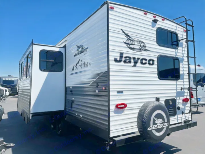 A white and gray Jayco travel trailer with slide-out extended, seen from the side/rear. A spacious RV rental option, ready for trips.. Jayco Jay Flight 2024