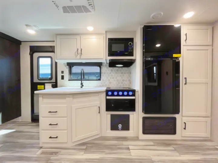 Modern RV rental kitchen interior featuring light cabinetry, black appliances (fridge, microwave, stove), and a sink.. Jayco Jay Flight 2024