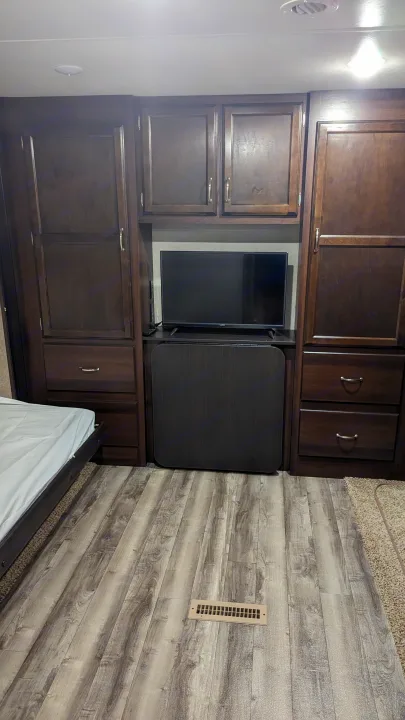 Compact RV rental bedroom: dark wood cabinetry, TV, bed, and floor vent. Optimized interior storage for travel.. Jayco Jay Flight 2018