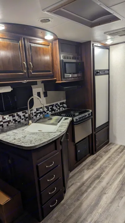 RV rental kitchen: a compact, modern interior with dark wood cabinets, stainless appliances, and a marble-patterned countertop.. Jayco Jay Flight 2018