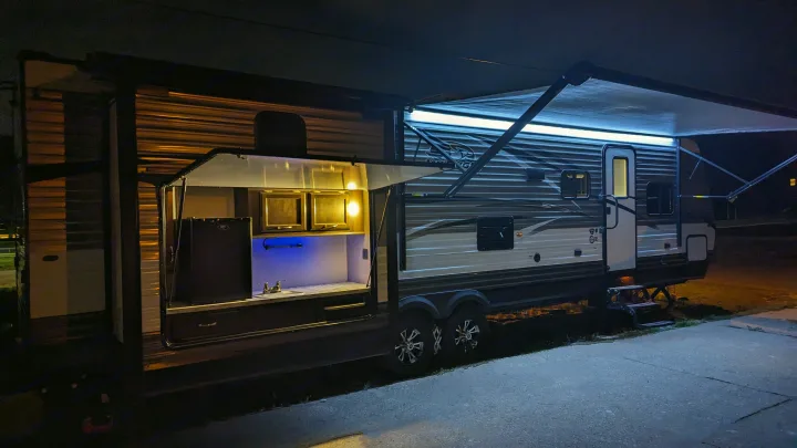 Nighttime RV rental: A bright travel trailer with an open, illuminated outdoor kitchen and lit awning, set for comfortable camping.. Jayco Jay Flight 2018