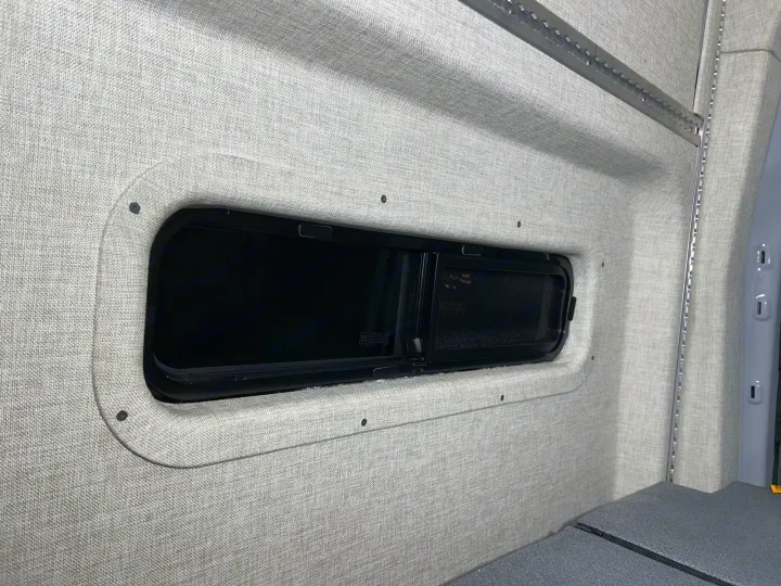 RV rental camper van interior featuring soft fabric walls, a modern window, and integrated L-track storage.. Ford Transit 2023