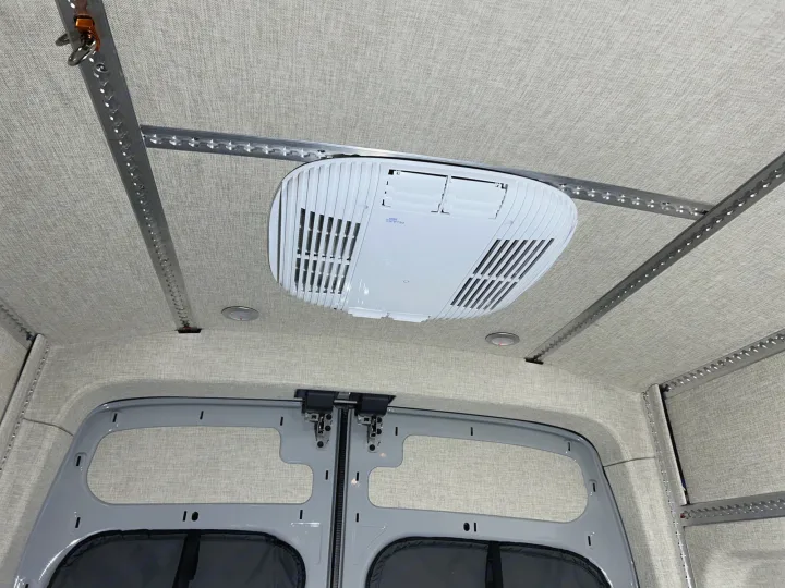 This RV rental interior features a clean fabric ceiling, versatile L-track rails, and a Dometic Belair 2800 AC unit.. Ford Transit 2023