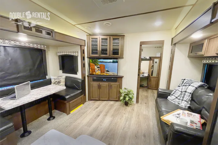 Cozy RV rental living space featuring a dining booth, TV, sofa, and access to a bunk bed area, with wood-look flooring.. Prime Time Crusader Lite 2020