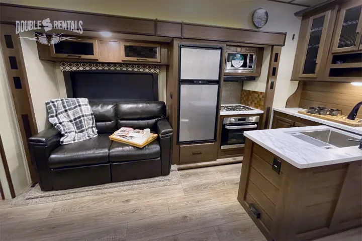 Modern RV rental interior featuring a full kitchen setup, refrigerator, cozy sofa, and stylish wood-look flooring.. Prime Time Crusader Lite 2020