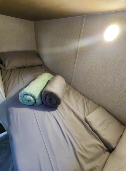 RV rental bunk bed with gray sheets, pillow, and two rolled blankets (green/gray) in a compact interior.. Other Other 2024
