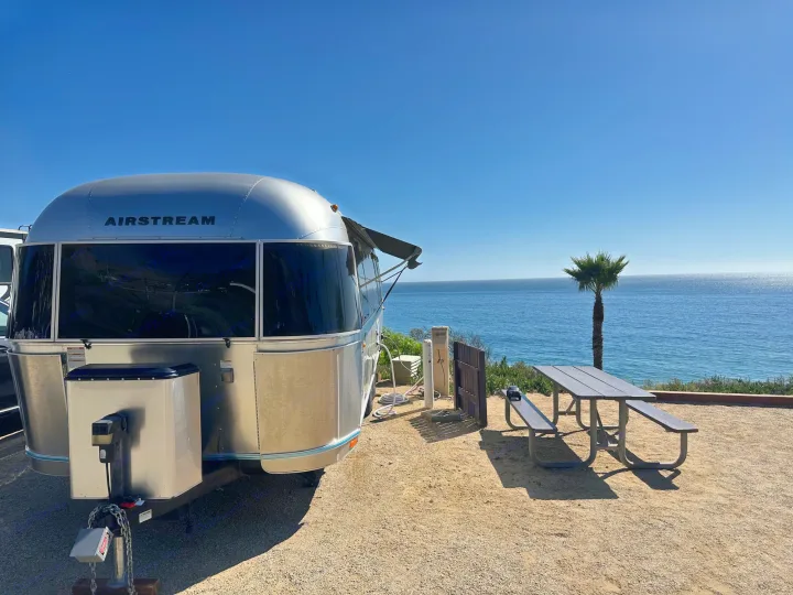 Stunning Airstream RV rental parked at an oceanfront campsite with a palm tree, picnic table, and blue sky.. Airstream Flying Cloud 2017