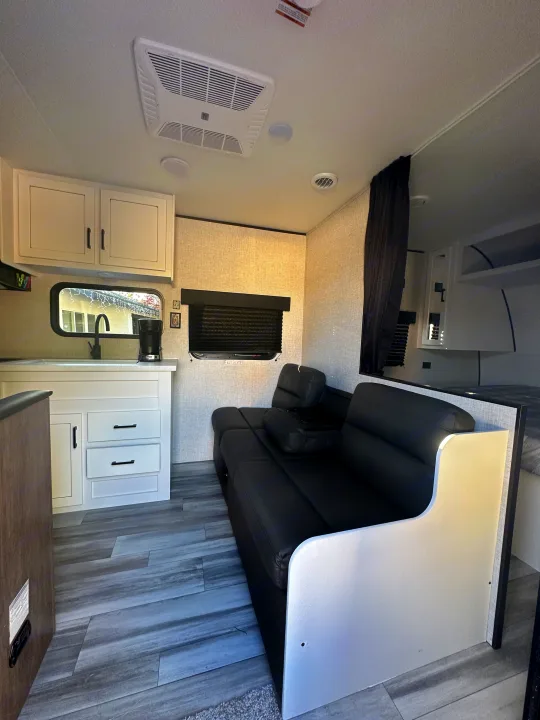 Inside an RV rental: a bright kitchen area with white cabinets, a sink, and a comfortable black leather sofa. Modern and practical design.. Other Other 2024