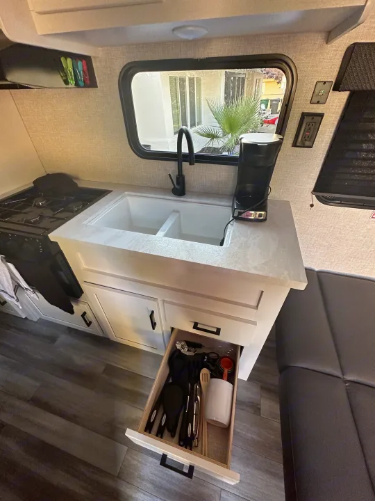 Clean RV kitchen: white counters, double sink, stove, coffee maker, and open utensil drawer. Great for an RV rental.. Other Other 2024