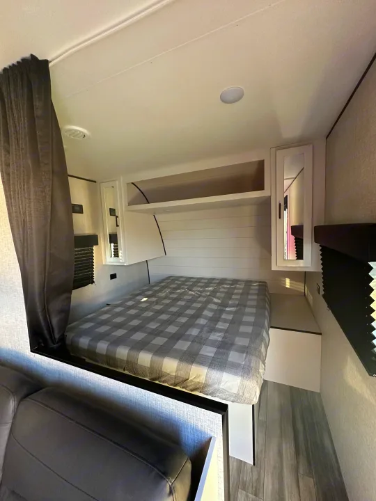 Cozy RV rental bedroom featuring a checkered bed, overhead storage, and integrated seating. Perfect for compact travel.. Other Other 2024