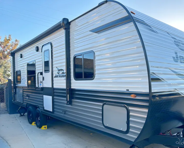 Grey & white Jay Flight RV rental, a spacious travel trailer parked outdoors. Features an awning, windows, and wheels with chocks.. Other Other 2024