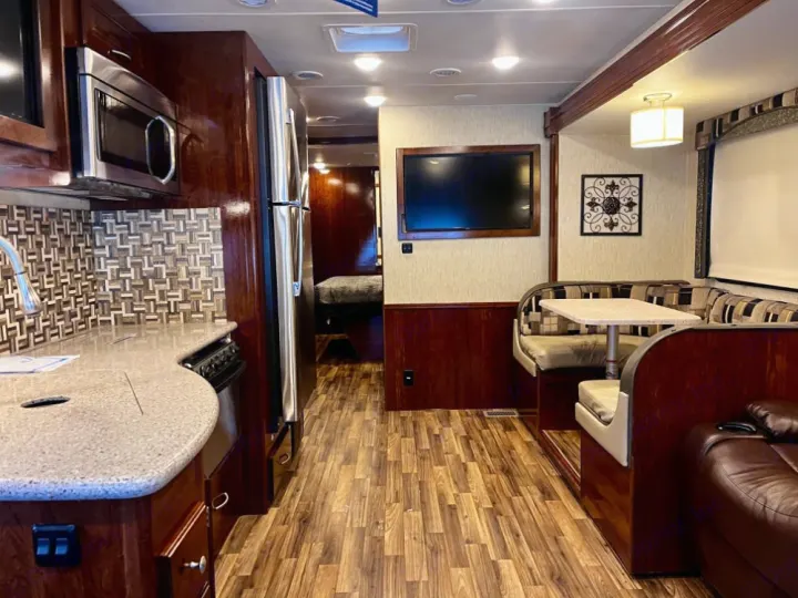 RV rental interior shows a full kitchen, dining booth, TV, and living area, featuring wood cabinetry and flooring.. Coachmen Mirada 2018