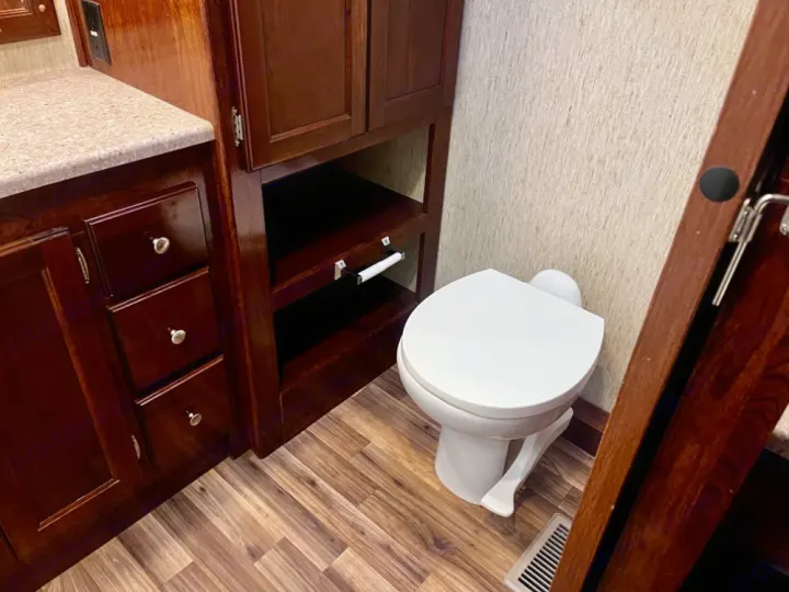 Inside an rv rental: a compact bathroom with a white toilet, wood vanity, and built-in storage shelves.. Coachmen Mirada 2018