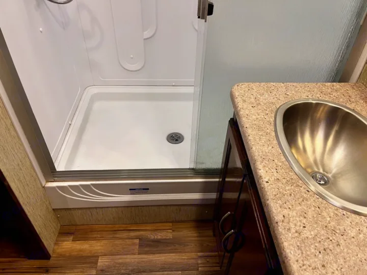 Inside an RV rental, a clean bathroom features a white shower stall and a counter with a shiny stainless steel sink.. Coachmen Mirada 2018