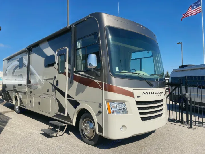 A large, beige and brown Mirada RV rental, a motorhome with steps extended, parked under a clear sky.. Coachmen Mirada 2018