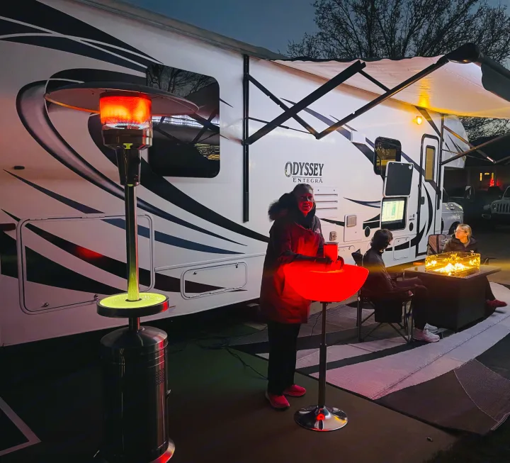 Evening RV rental gathering with a patio heater, glowing table, and warm fire pit creating a cozy ambiance.. Entegra Coach Odyssey 2020