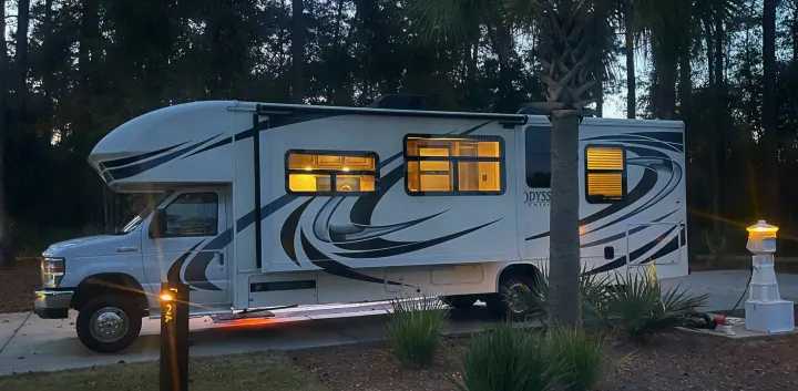 An Odyssey rv rental motorhome at campsite 24 at night, with interior lights on and connected.. Entegra Coach Odyssey 2020