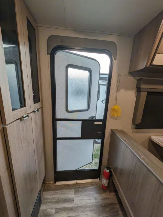 RV rental interior: open screen door, wood cabinets, dinette bench, and visible fire extinguisher.. Grand Design Imagine XLS 2021