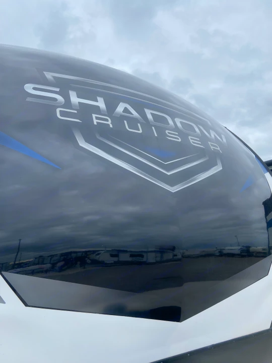 Close-up of a sleek black and white Shadow Cruiser RV's front, perfect for RV rental, reflecting cloudy skies.. Cruiser RV Shadow Cruiser 2022
