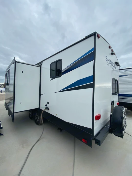 White travel trailer RV rental with a slide-out extended and blue accents, parked outdoors under a cloudy sky.. Cruiser RV Shadow Cruiser 2022